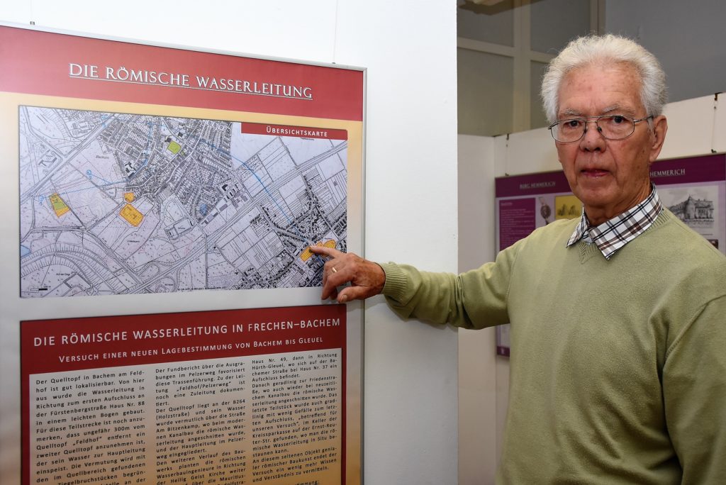 Josef Bucco zeigt auf die Sparkasse in Hürth-Gleuel, in der ein Stück römische Wasserleitung zu sehen ist.